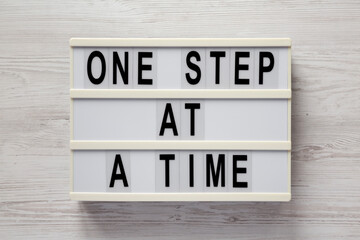 'One step at a time' on a lightbox on a white wooden surface, top view. Flat lay, overhead, from...