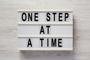 'One step at a time' on a lightbox on a white wooden surface, top view. Flat lay, overhead, from above.