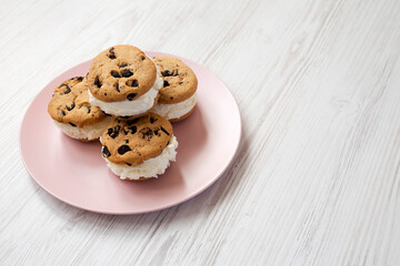 Homemade Chocolate Chip Cookie Ice Cream Sandwich on a pink plate on a white wooden background, side view. Space for text.
