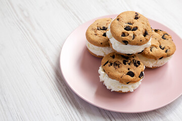 Homemade Chocolate Chip Cookie Ice Cream Sandwich on a pink plate on a white wooden background, side view. Copy space.