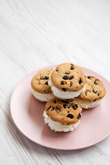 Homemade Chocolate Chip Cookie Ice Cream Sandwich on a pink plate on a white wooden surface, side view. Copy space.