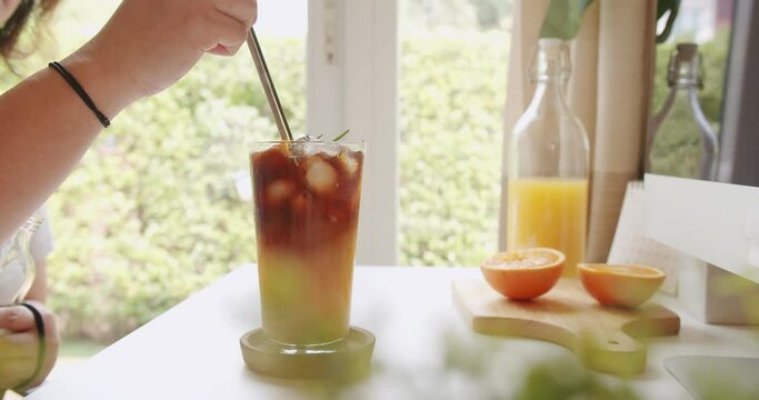 Person hand holding twisting straw in glass of juice on workspace, tropical beverage refreshment in summertime.
