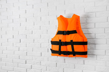 Orange life jacket on white brick wall. Space for text