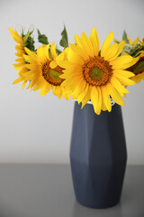 Bouquet of beautiful sunflowers on table near light wall