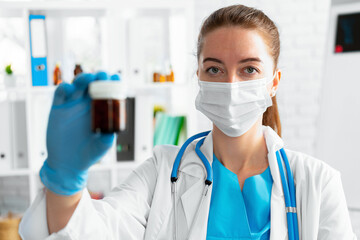 Female doctor in mask holding glass jar with medicine