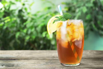 Delicious iced tea in glass on wooden table outdoors, space for text