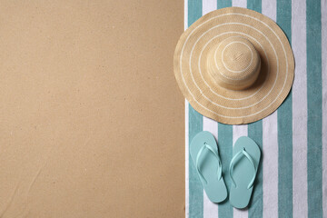 Straw hat, flip flops and space for text on beach sand, top view. Summer vacation