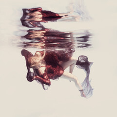 A woman in a red dress with ribbons and airy fabric poses underwater against a light background as if in zero gravity.