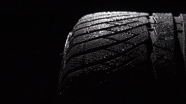 Sports Tire in Water Droplets. Loop. The geometric pattern of the wheel in water droplets slowly rotates towards the viewer. Drops sparkle on the black rubber on a black background