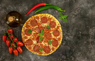 Obraz na płótnie Canvas Tasty pepperoni pizza and cooking ingredients tomatoes, chili, basil on dark background.