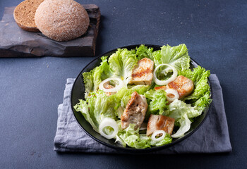 Salad of lettuce leaves and turkey meat on a plate on a black background, close-up.