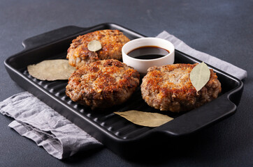 Homemade beef cutlets on a black cast-iron pan with lavrushka leaves on a black background, close-up.