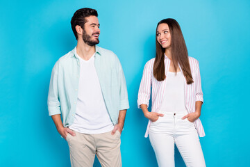 Photo of shiny sweet young lovers dressed casual shirts looking each other hands arms pockets isolated blue color background