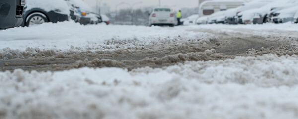 Muddy splush on wet urban road with car track on parking lot