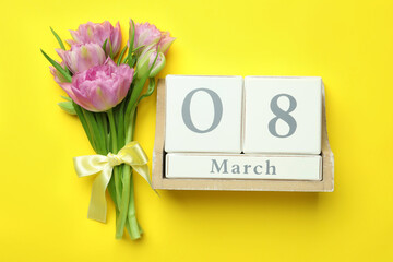 Wooden block calendar with date 8th of March and tulips on yellow background, flat lay. International Women's Day