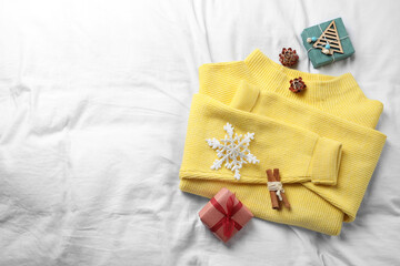 Obraz na płótnie Canvas Yellow warm sweater and decorations on white bedsheet, flat lay. Space for text