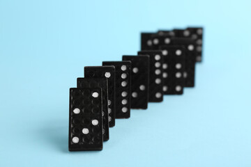 Black domino tiles falling on light blue background