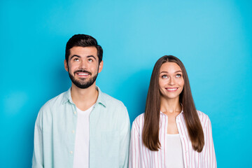 Photo of cheerful attractive spouses look empty space above good mood isolated on blue color background