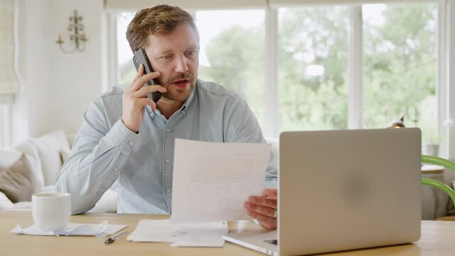 Man on phone call at home with laptop computer reviewing domestic finances  - shot in slow motion