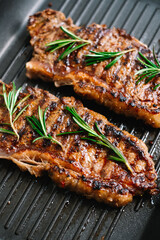 Grilled beef steak with rosemary in black grill pan on the table.