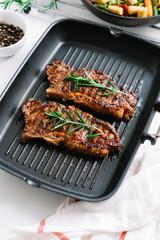 Grilled beef steak with rosemary in black grill pan on the table.