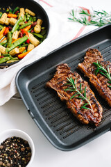 Grilled beef steak with vegetables and rosemary in black grill pan on the table.