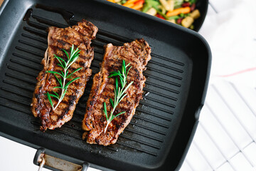 Grilled beef steak with rosemary in black grill pan on the table.