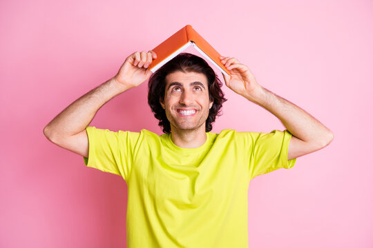 Photo of cheerful optimistic young clever man look read book above head nice smile isolated on pastel pink color background