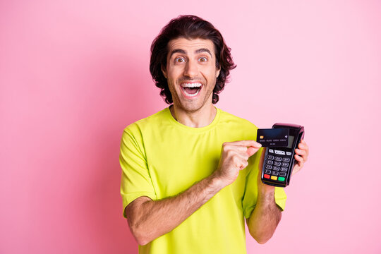 Photo of charming amazed young man hold credit card swipe reader isolated on pastel pink color background