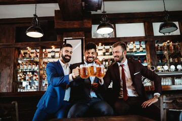 Handsome businessmen are drinking beer, talking and smiling while resting at the pub