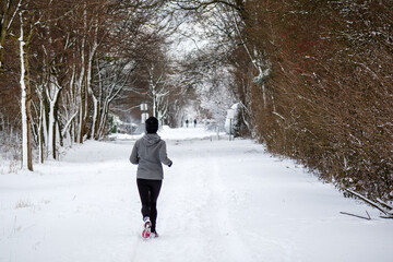 woman running in the snow between rows of trees