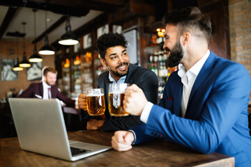 Happy young businessmen drinking beer and talking at pub after work