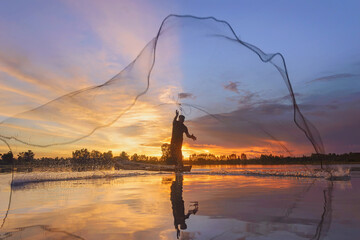 Fisherman casting his net on during sunrise.Silhouette Asian fisherman on wooden boat casting a net for freshwater fish