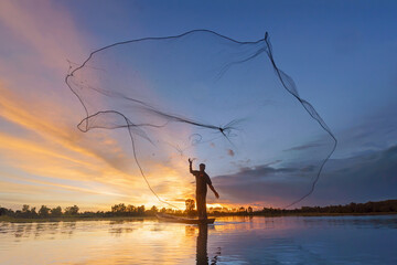 Fisherman casting his net on during sunrise.Silhouette Asian fisherman on wooden boat casting a net for freshwater fish