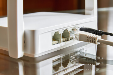 White wireless router on a glass table connected by cable to the Internet. Close-up
