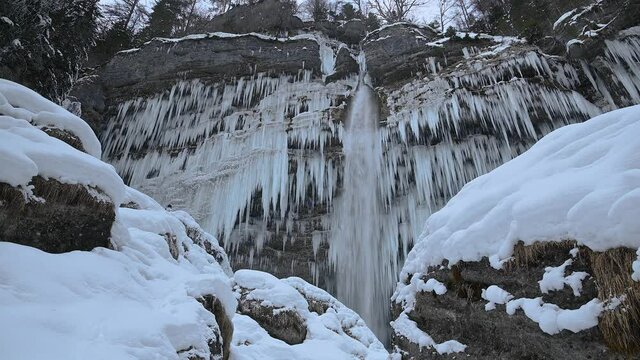 People taking photos of famous waterfall in Slovenia. Peričnik waterfall in cold weather. Huge thick icicles hanging from cliff in Alps mountains. Very cold winter scene. Static shot, wide angle