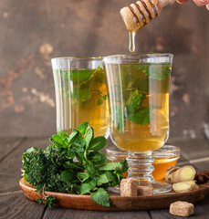 Warm herbal drink infusion in glasses for cold days. Two cups of ginger tea with mint, thyme and honey on a wooden table.