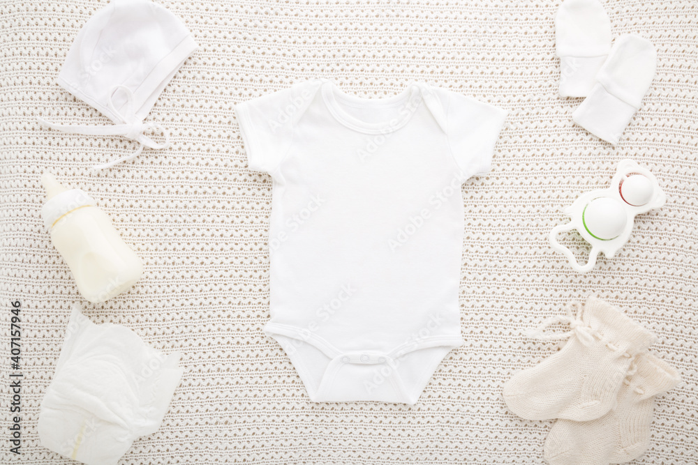 Wall mural newborn white bodysuit, hat, mittens, socks, diaper, milk bottle and rattle toy on light blanket bac