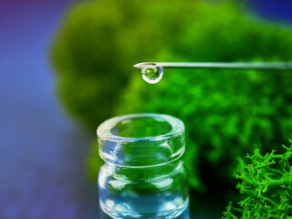 Medical bottle, drop on a needle in the background moss. The concept of science and nature