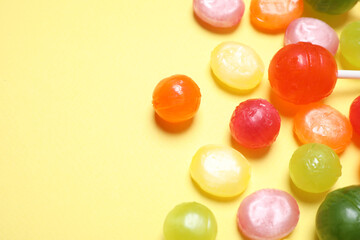 Many different hard candies on yellow background, closeup. Space for text