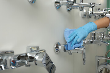 Woman cleaning faucets with rag in bathroom fixtures store, closeup
