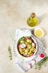 Tasty hot potato salad with green beans, fresh radishes and herbs dressing with olive oil and mustard sauce, light background.