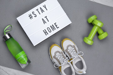 Naklejka premium Sport equipment and lightbox with hashtag STAY AT HOME on grey yoga mat, flat lay. Message to promote self-isolation during COVID‑19 pandemic