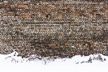 Grunge red dirty brick wall. Urban underground texture. Antique house exterior wall. Vintage rustic building architecture. Winter brick wall. Snow on the ground.