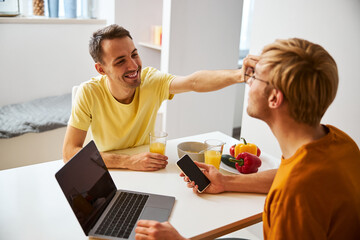 Happy gay couple having breakfast and using modern gadgets