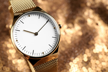 Luxury wrist watch on gold paillette background, closeup. Space for text