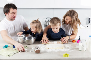 A young family with two small children in the kitchen are preparing cookie dough and laughing. The pleasure of spending time together. Love and tenderness.