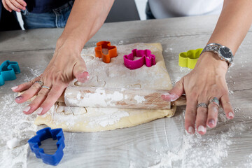 Women's hands in jewelry roll out the dough. Top view.