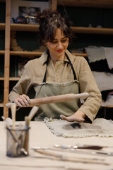 A beautiful Caucasian woman looks to the side and makes dishes with her own hands in a pottery workshop. Pottery made of clay with their own hands. Manual labor