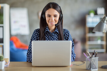 Photo of young beautiful attractive focused smiling positive businesswoman in headphones typing in...